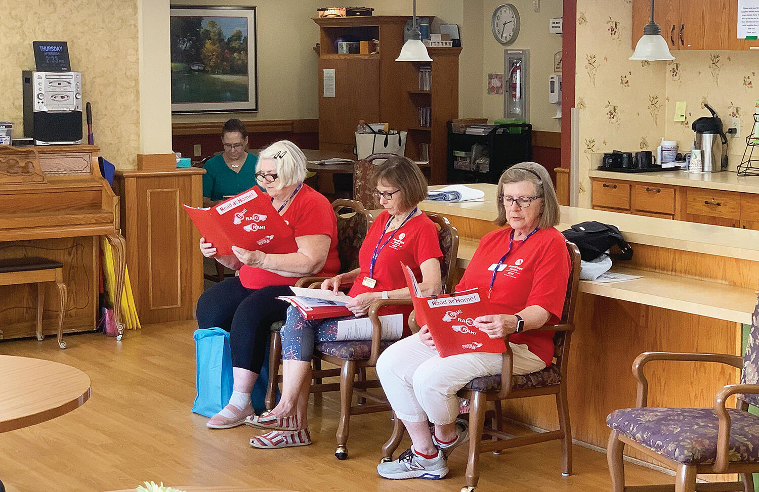 A trio of AmeriCorps Seniors RSVP, Readers Theater volunteers consisting of Lucinda McCoy (left), Franic Karpen (middle), and Jane Erickson (right) performed for residents at Park Terrace, in Buffalo, where the group reads to residents every third Thursday of each month. Pictured in the background is AmeriCorps Seniors RSVP Program Coordinator Amy Johnson. (Photo by Mike Gesellchen)