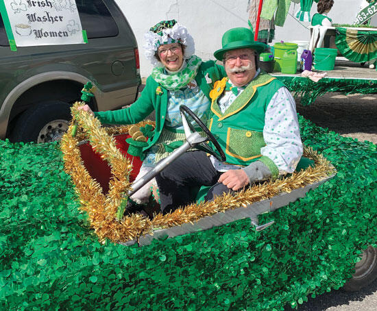 Trisha and Fred, of The Costume Shoppe in Maple Lake, ride in a car decorated with sparkling shamrocks and gold tinsel.